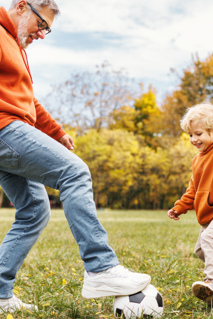 Grandfather playing soccer in field with young grandchild.