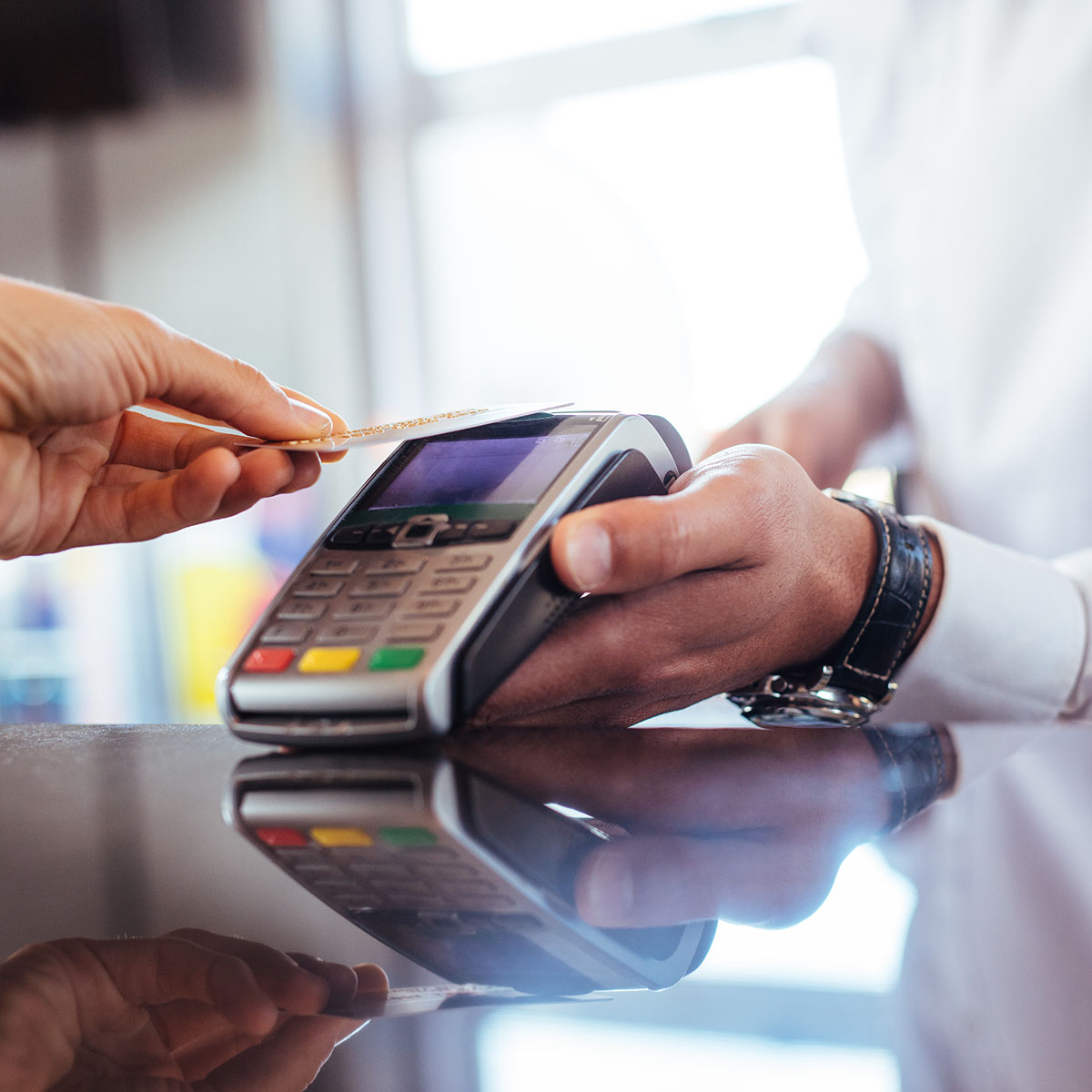 Hand of customer paying with contactless credit card with NFC technology. Bartender with a credit card reader machine at bar counter with female holding credit card. Focus on hands.