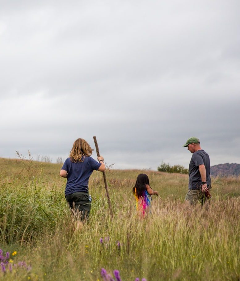 Family of three hiking up a mountain path. There is a son, daughter and dad walking through a grassy hilled area towards a dramatic sky.