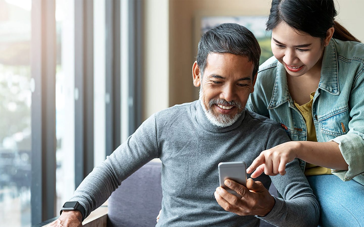 Man and woman smiling, looking at the screen of a mobile phone together
