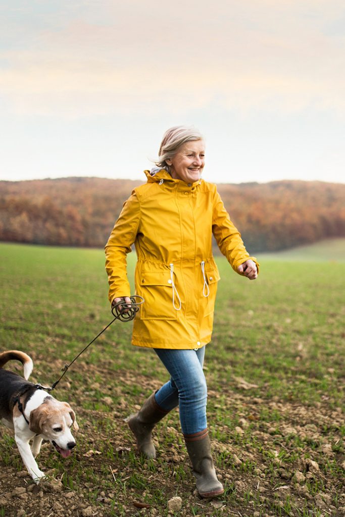 Active senior woman with dog on a walk in a beautiful autumn nature.