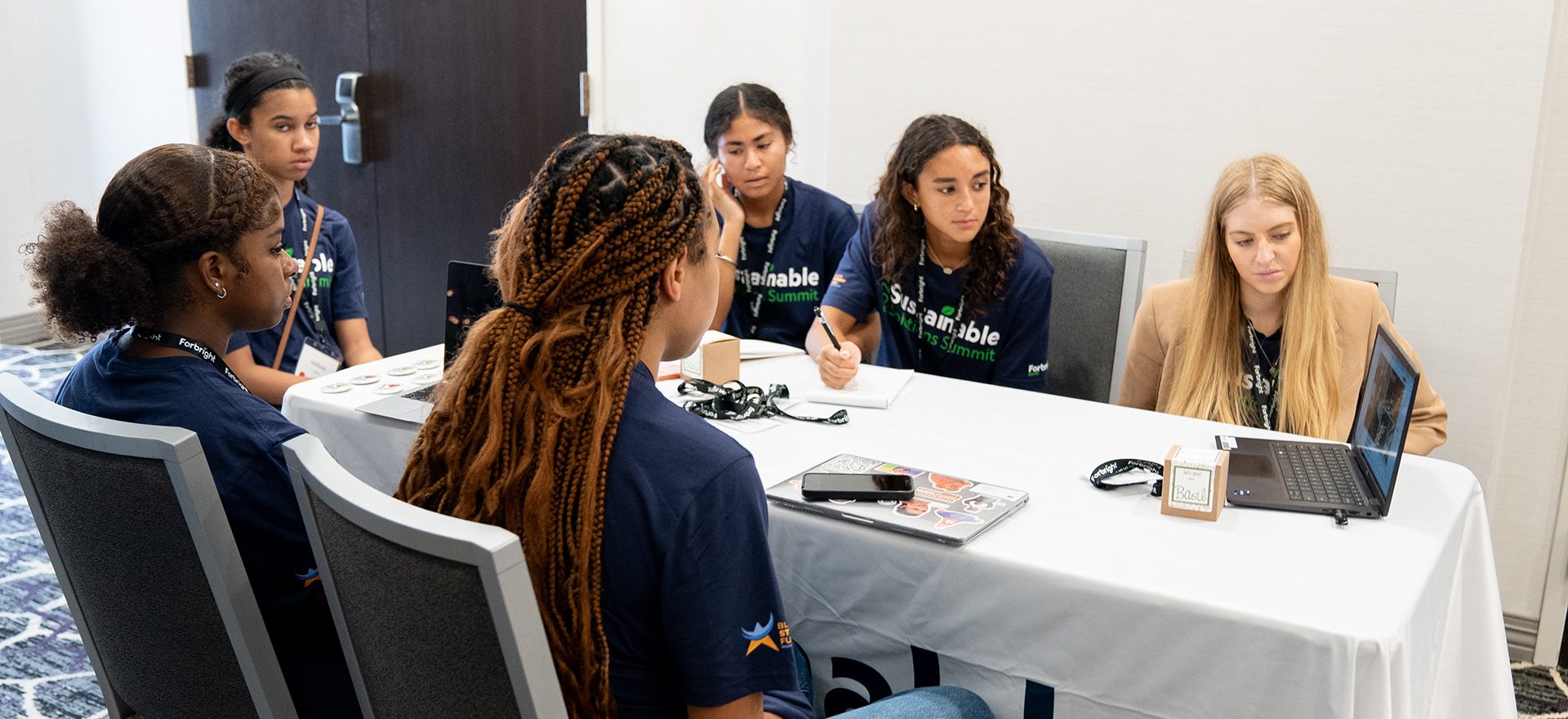 A group of students around a table all watching something on a laptop computer