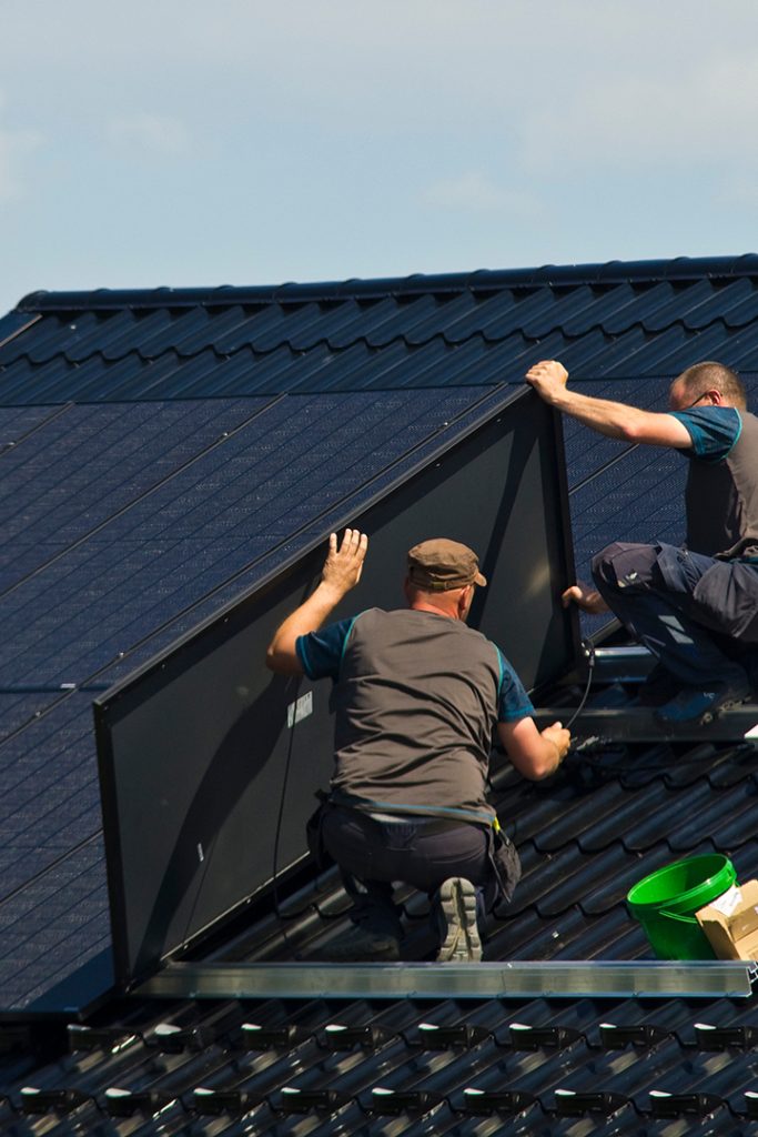 Two workers install solar panels on roof..