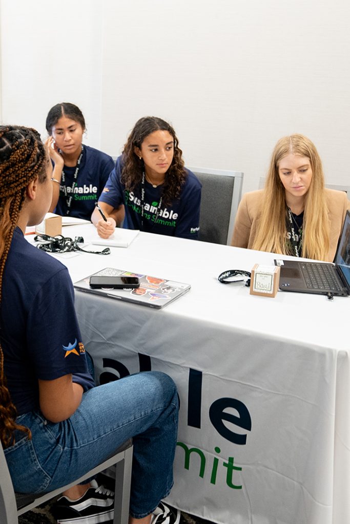 A group of students around a table all watching something on a laptop computer