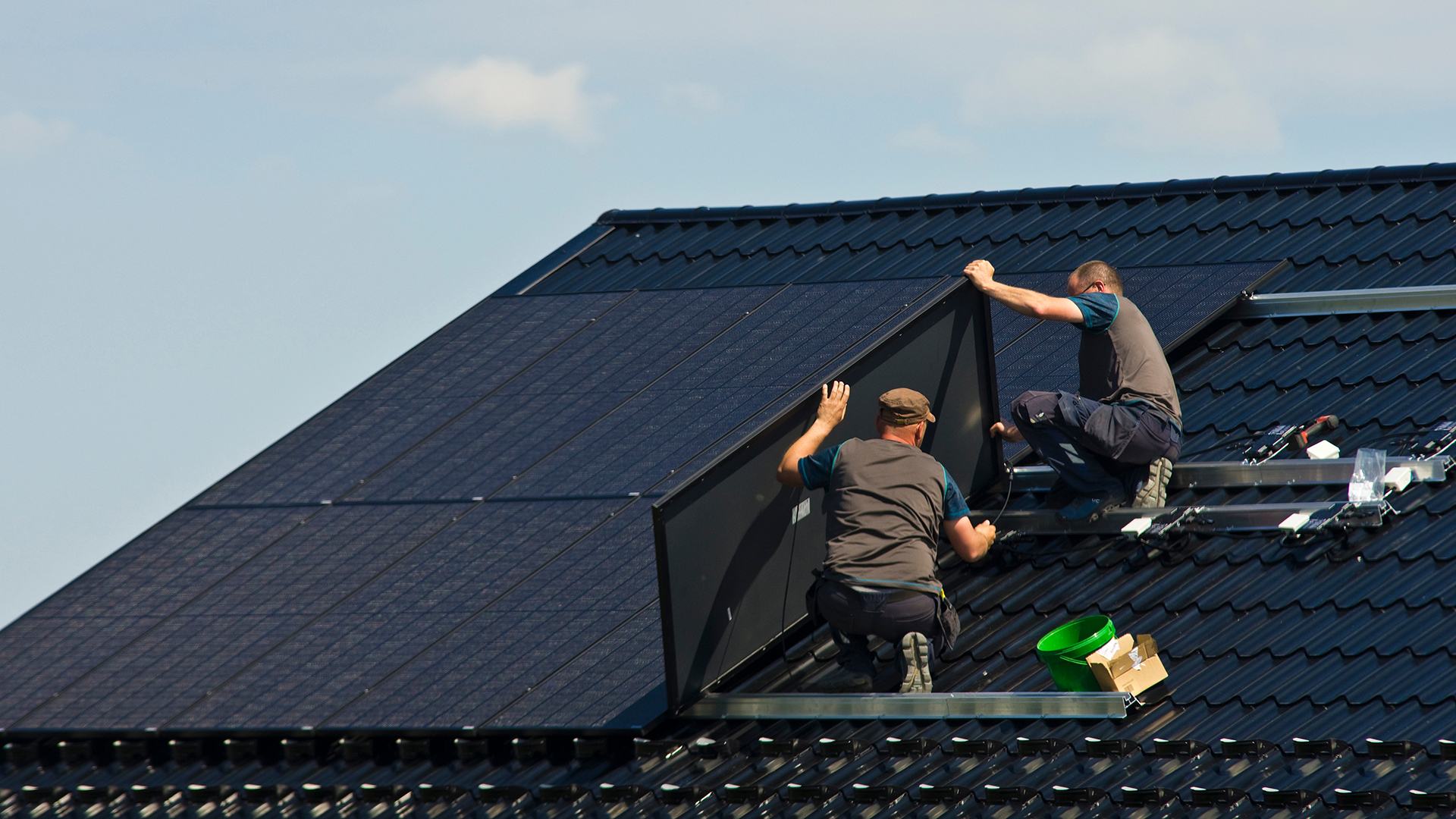 Two workers install solar panels on roof..