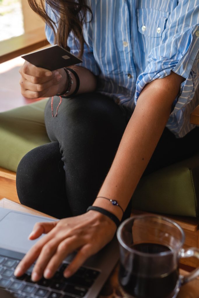 Woman's hand typing on a keyboard while she holds a credit card with the other hand.