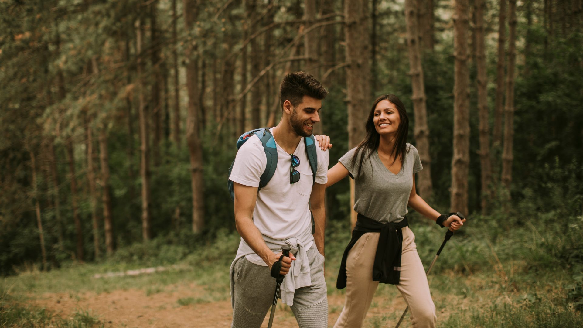 Couple of young hikers with backpacks walking through the forest