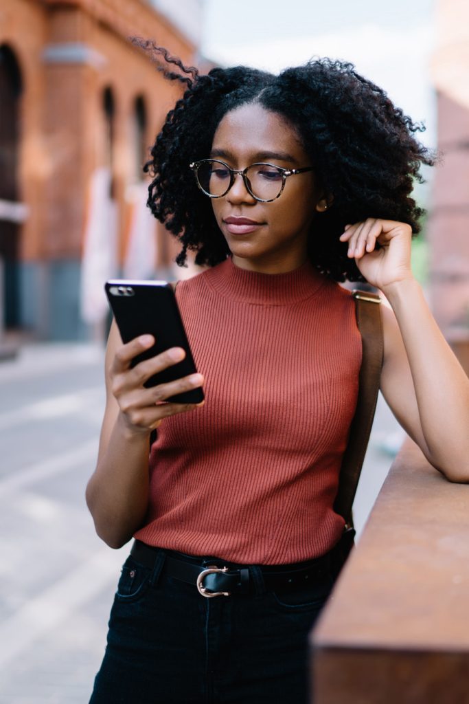 A young Black woman using smartphone while standing outdoors .