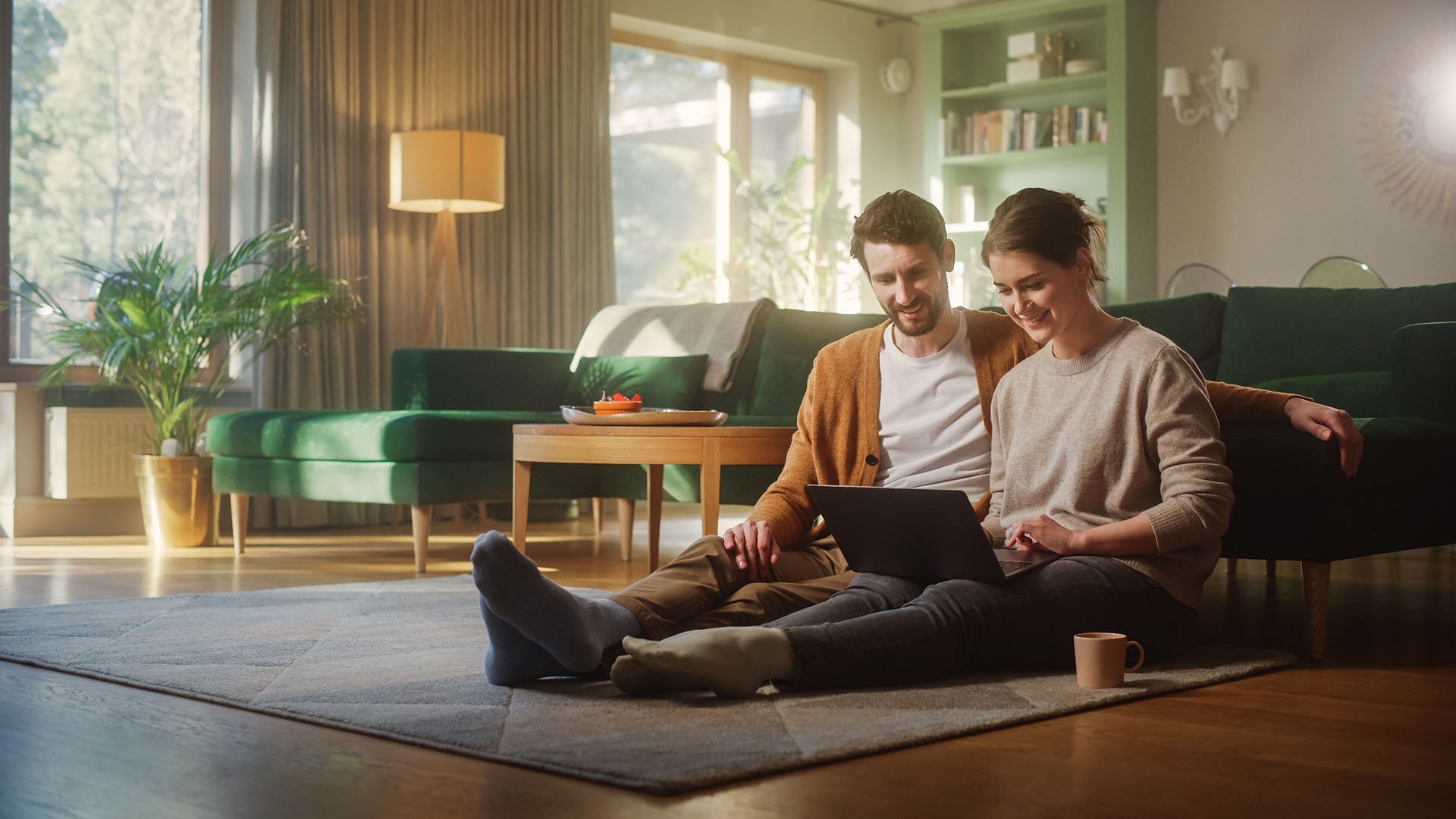 Couple use laptop computer while sitting on the living room floor room of their apartment.