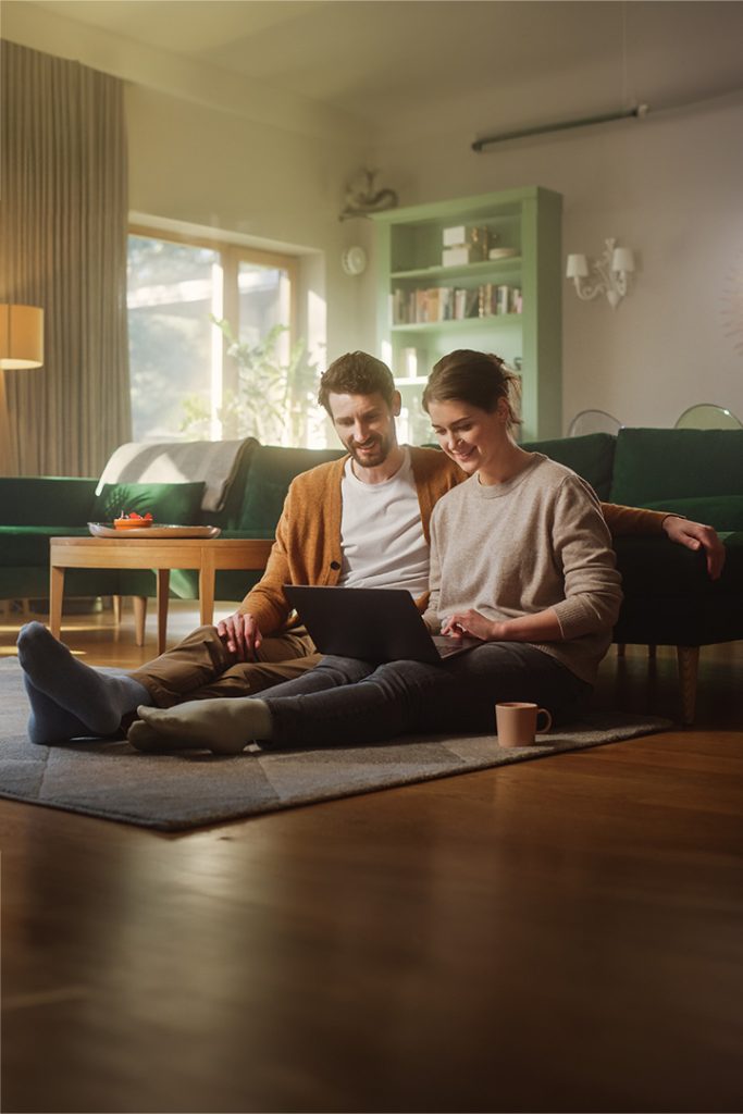 Couple use laptop computer while sitting on the living room floor room of their apartment.