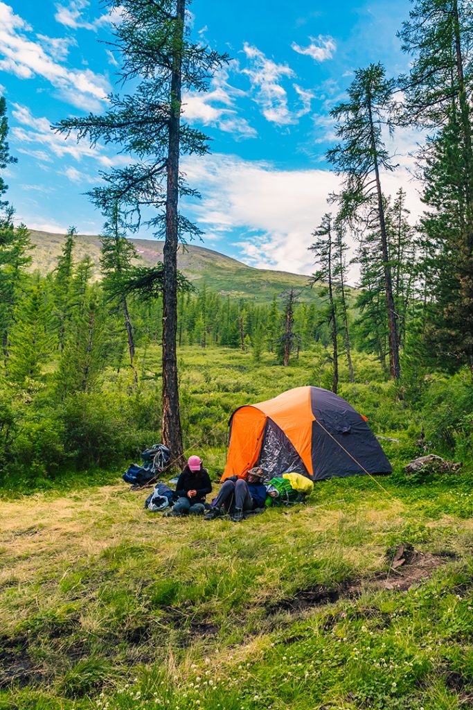 An orange tent in the woods with friends camping.