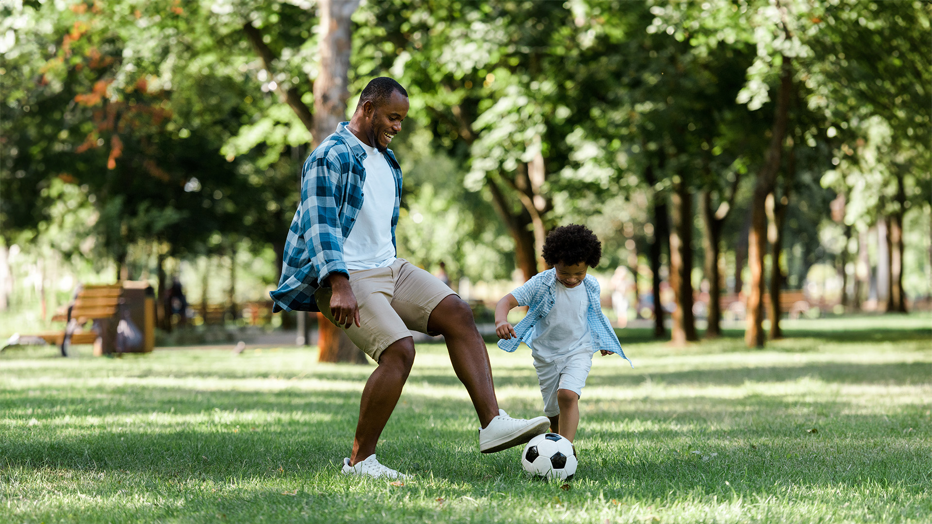 A Black man and his son play soccer in a grassy field.