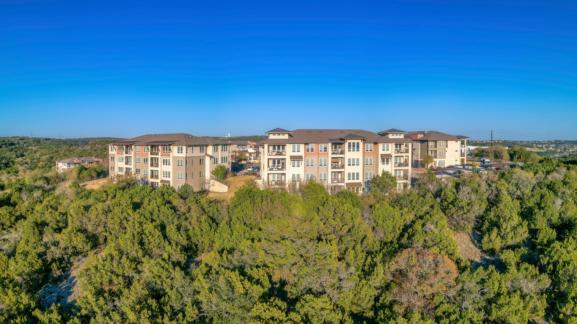 Apartment complex near the tree forest. There are trees on the slope at the front and a background of clear blue sky background.