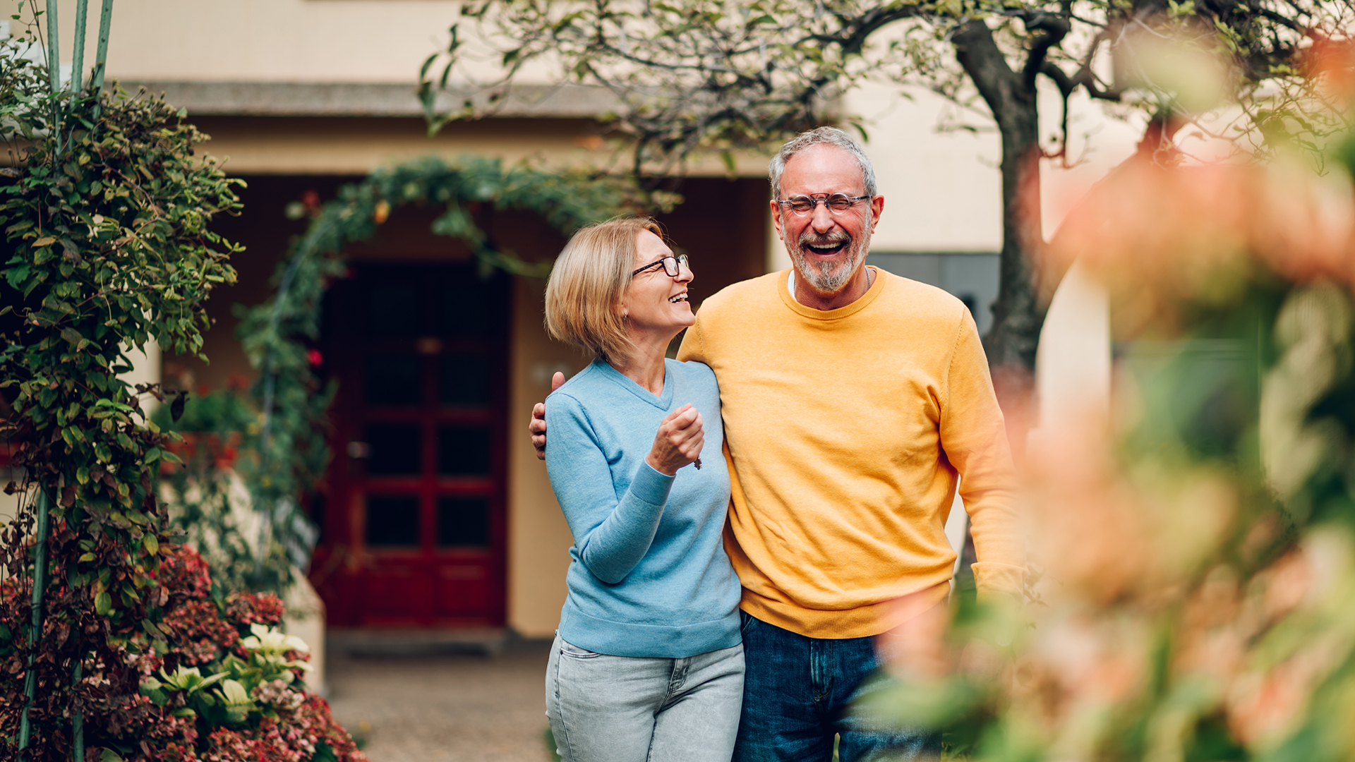 Portrait of senior retired couple laughing and walking together in a garden outside a home.