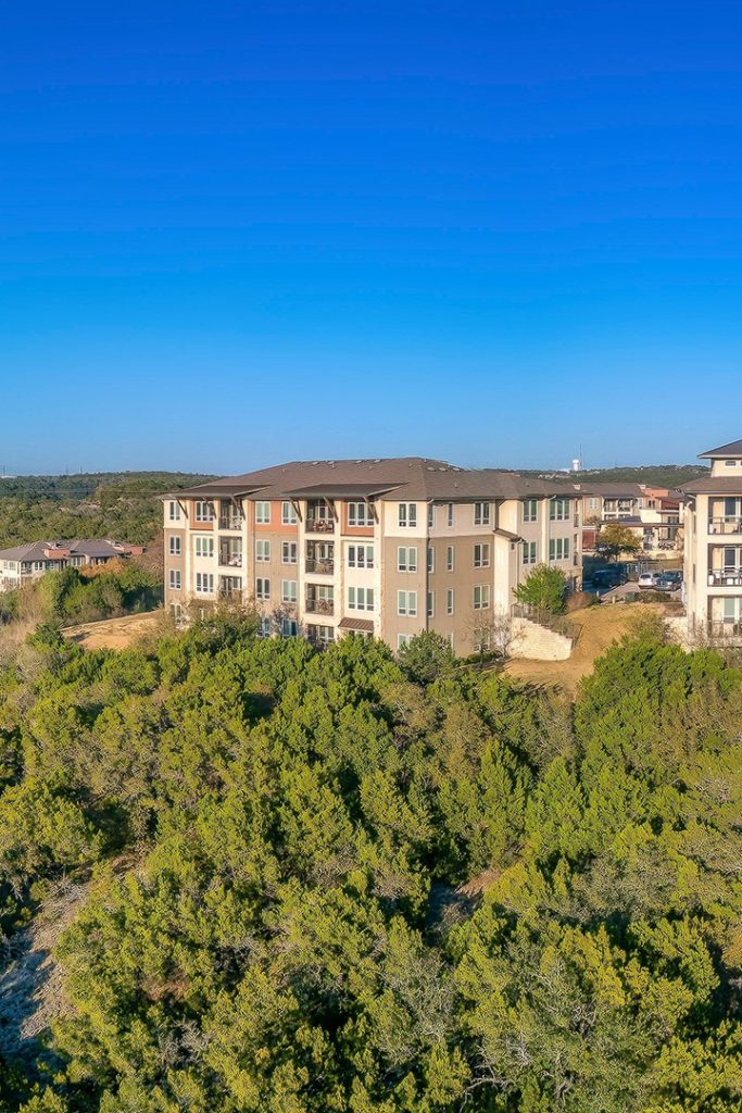 Apartment complex near the tree forest. There are trees on the slope at the front and a background of clear blue sky background.