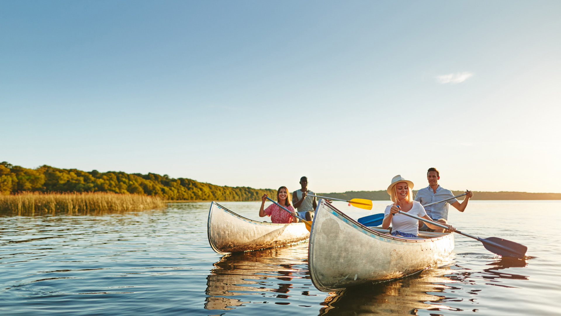 A group of friends canoeing on a lake with the sun setting behind them.
