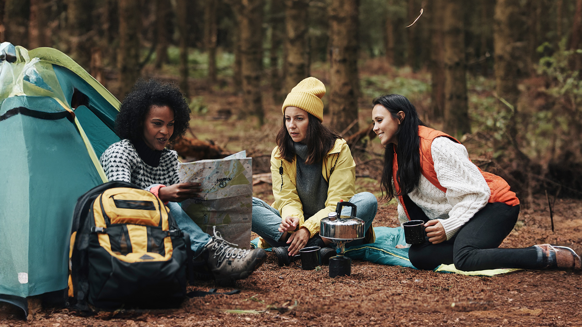 A group of female friends sitting outside of a tent on a camping trip.