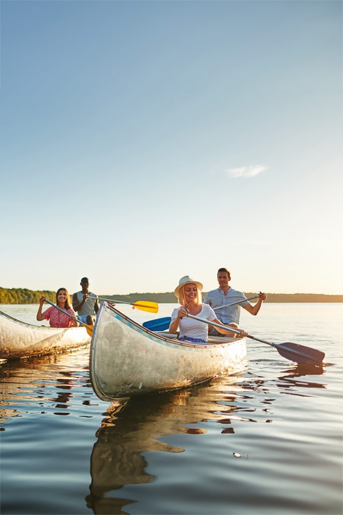 A group of friends canoeing on a lake with the sun setting behind them.