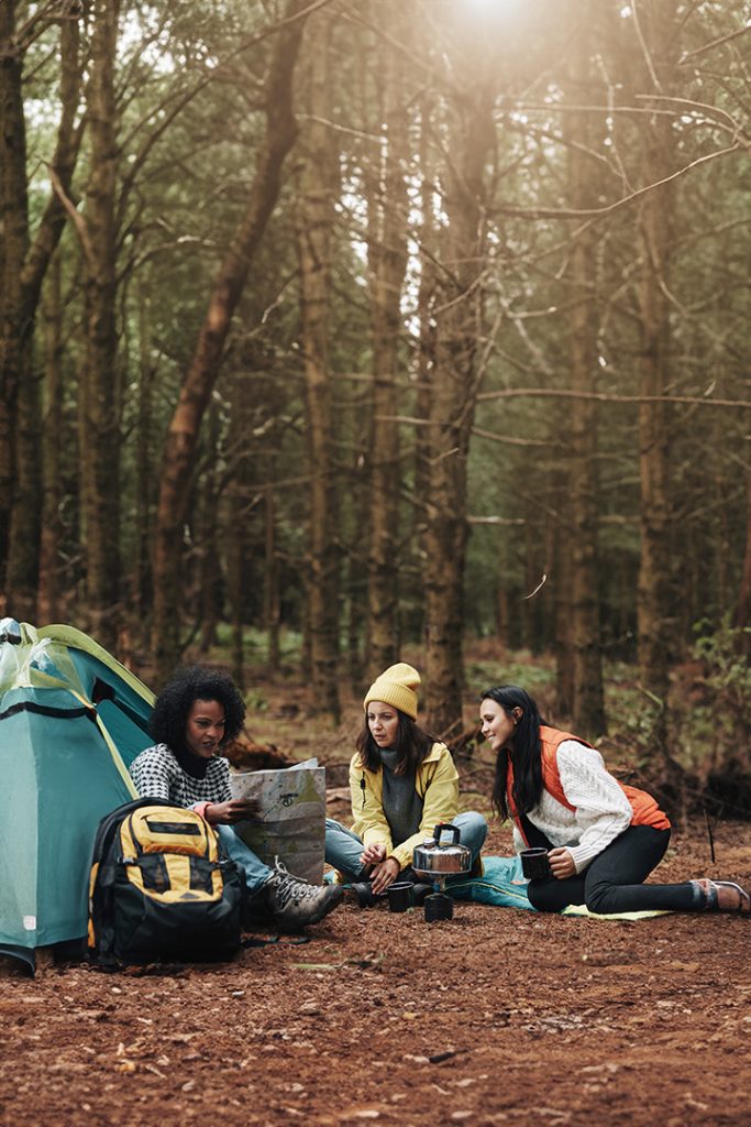 A group of female friends sitting outside of a tent on a camping trip.