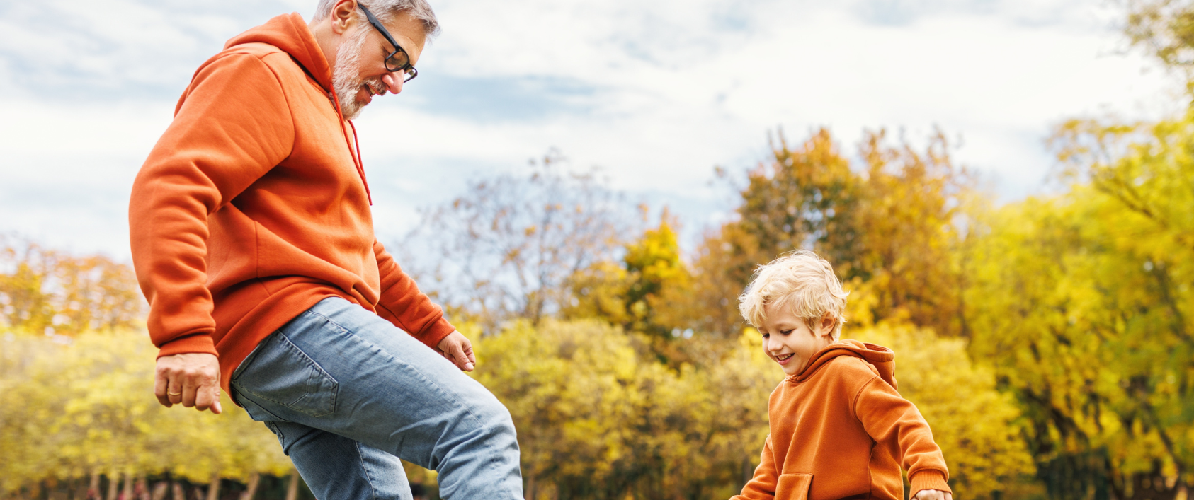 Grandfather playing soccer with young grandchild in field.