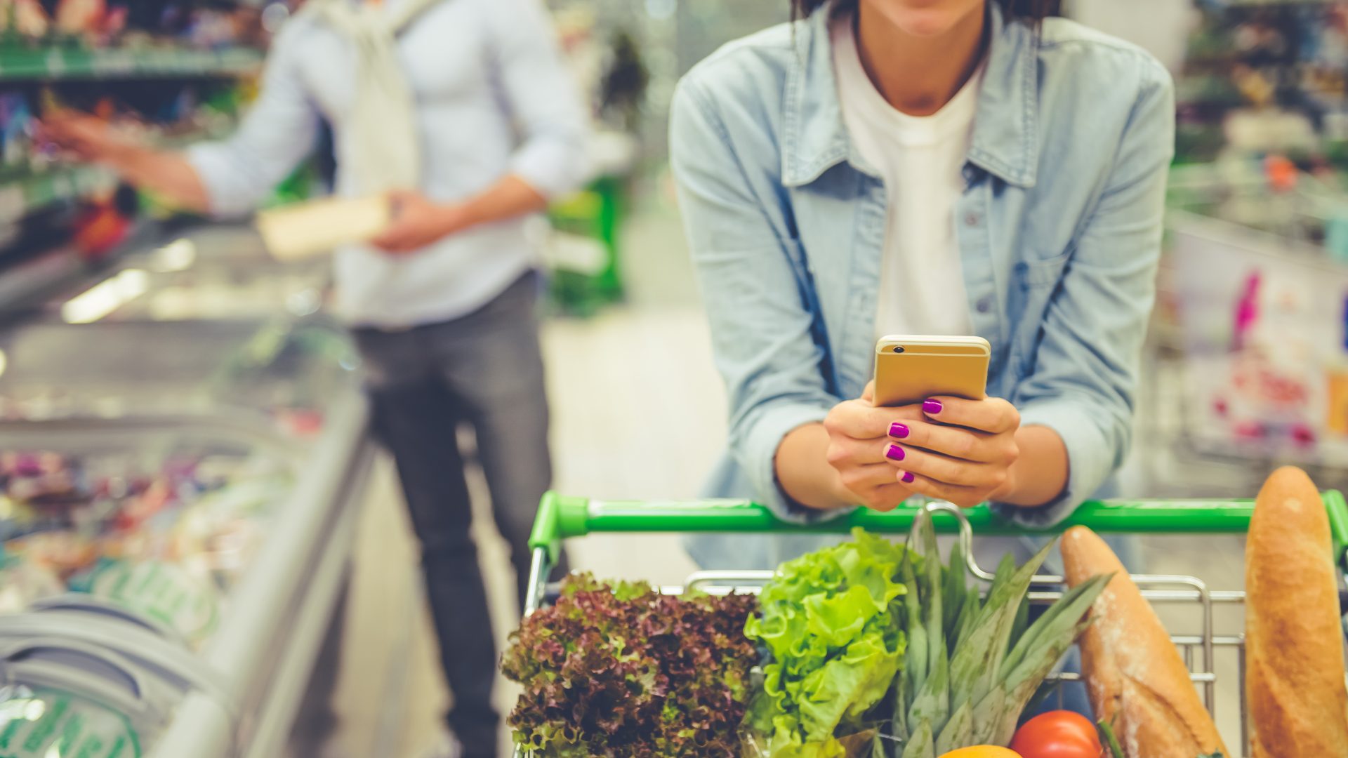 Woman on phone shopping for groceries.